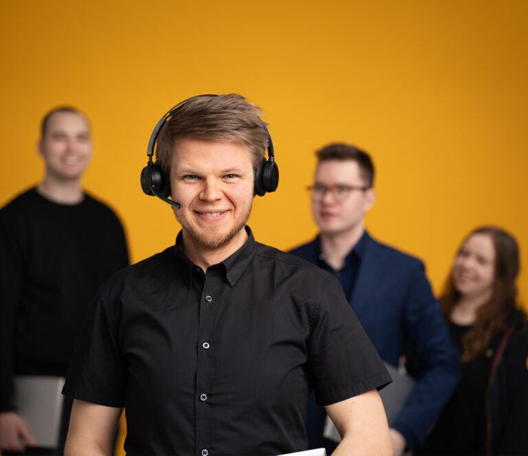 Vetonaula IT-tukitiimi: etualalla kuulokemikrofonilla varustettu asiantuntija, taustalla kollegoita