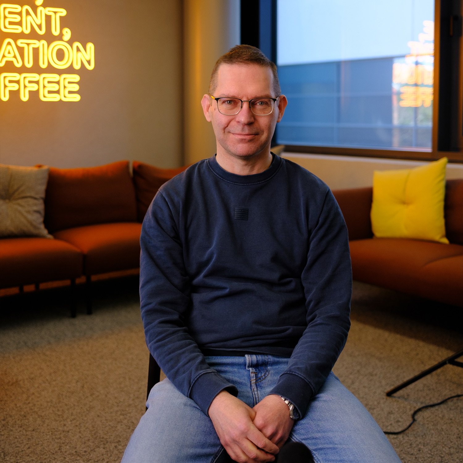 Silmälasipäinen mies istuu rennosti toimiston lounge-tuolissa